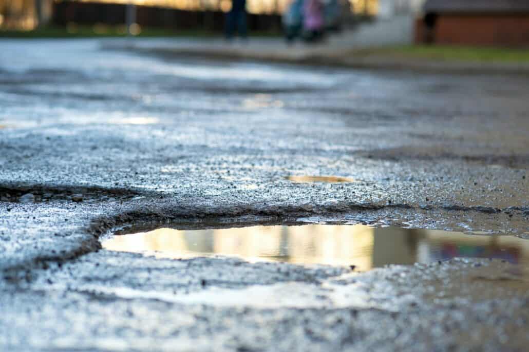 Close up of a road in very bad condition with big potholes full of dirty rain water pools